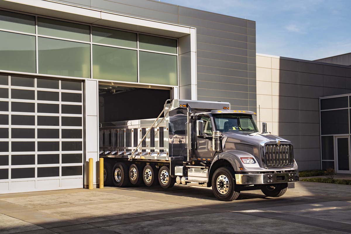 Silver and chrome International HX Dump Truck with new logo badge on front. Dramatic lighting. Truck pulling out of a truck bay in the sun. 