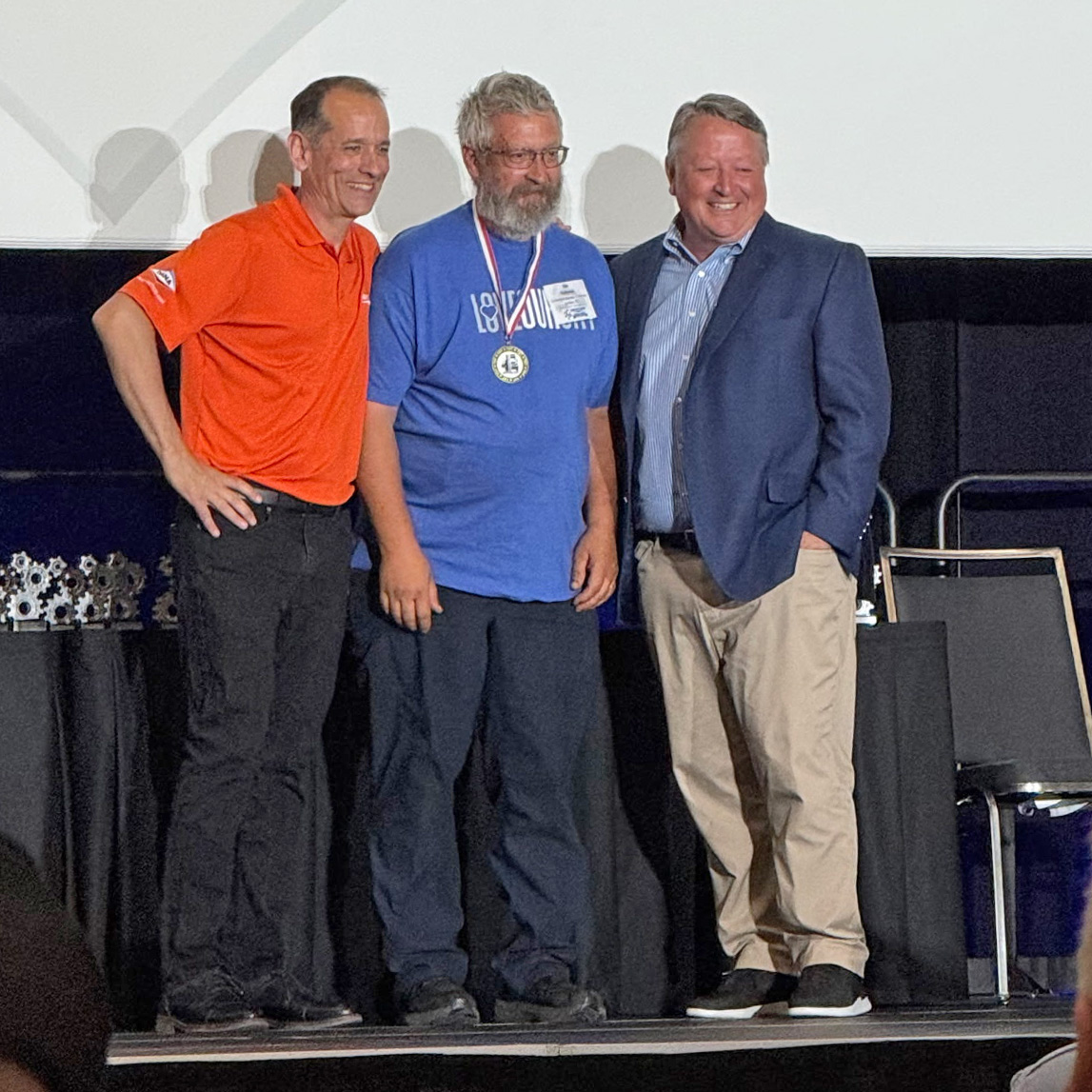 Ken Holleman stands on stage being presented with the Grand Championship Title for the Idealease IdealTECH Skills Competition in 2026 in Indianapolis, IN.